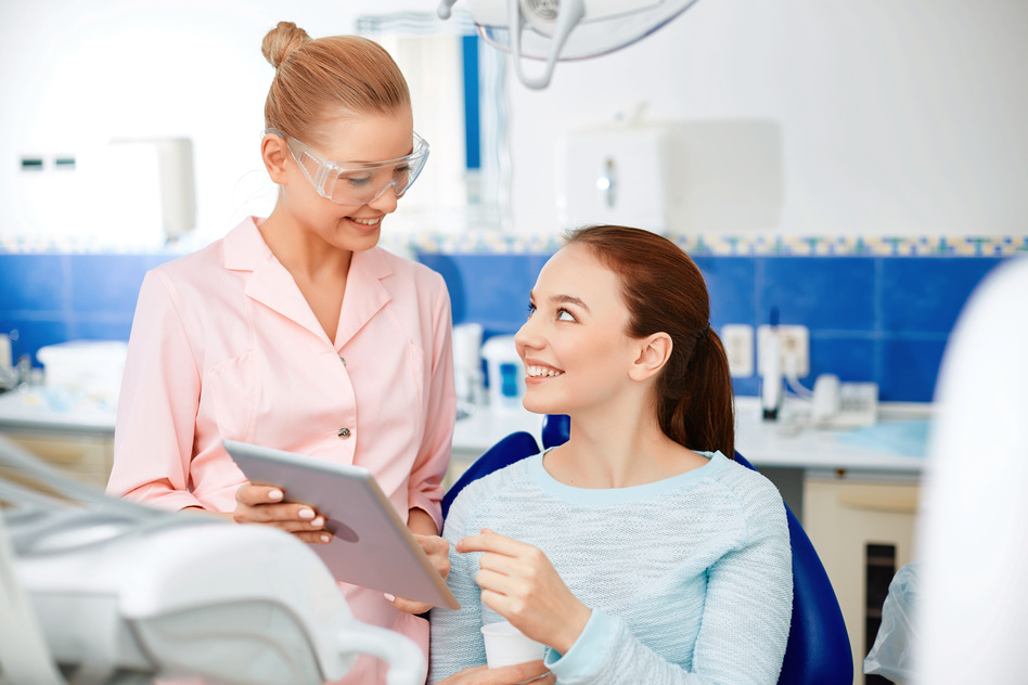 Young dentist with touchpad explaining her patient new method of healing teeth